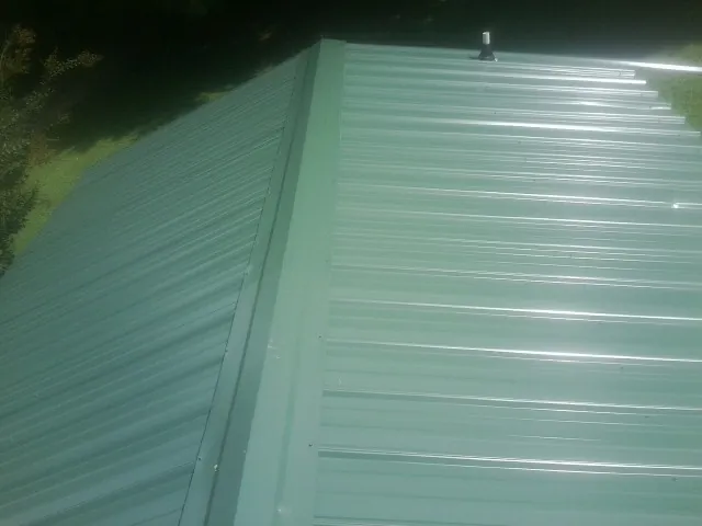 New green metal panels meeting at the ridge of a roof — Flat Roof Repair work by our crew in Voorhees