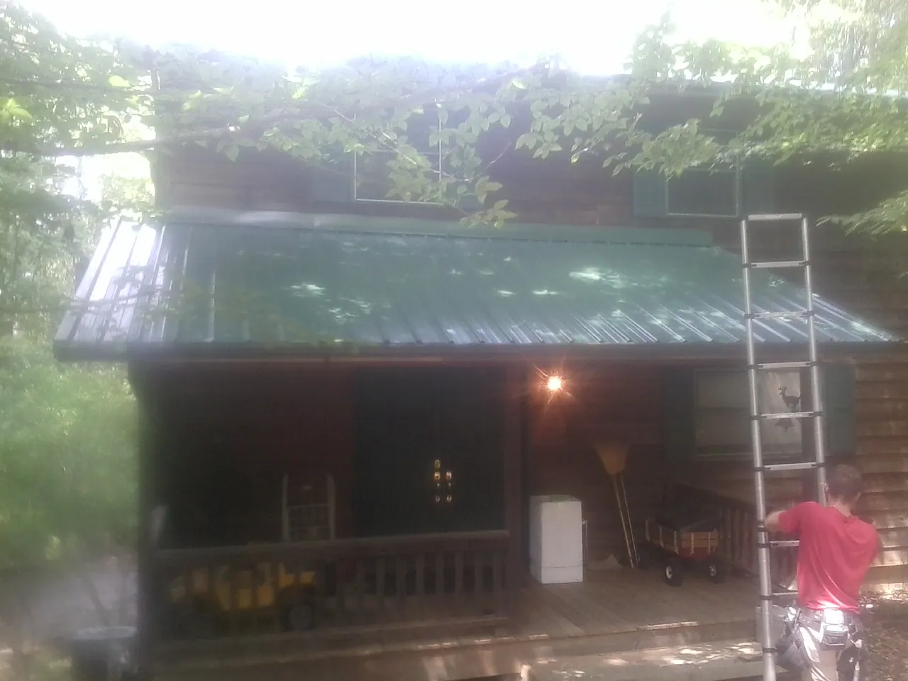 Worker on a ladder at the green porch roof of a wooded cabin in Voorhees
