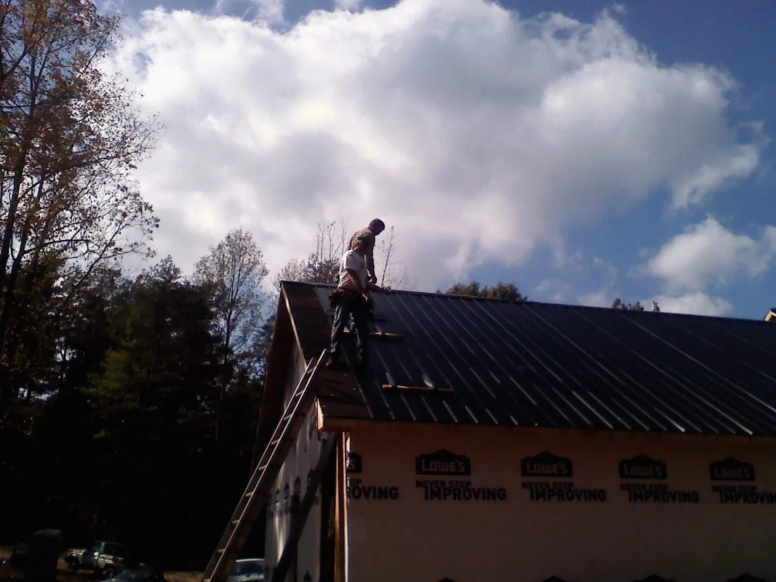 Roofer fastening dark metal panels high against a cloudy sky, from a Roof Inspection job in Voorhees