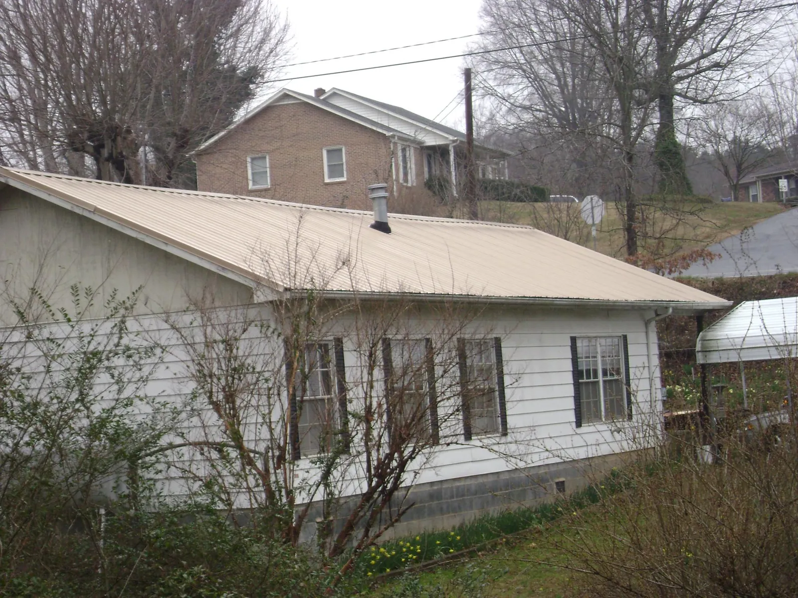 Tan metal roof on a white sided house set into a hillside — Commercial Roofing by Roofing Brothers in Voorhees